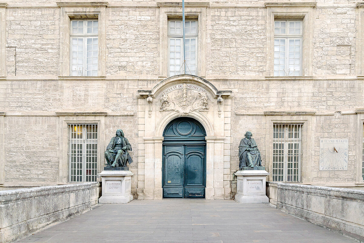 View of ancient stone facade and entrance with carved pediment of oldest faculty of medicine in the world still in operation, Montpellier, France
